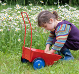 Ein kleines Kind hockt in der Wiese vor dem roten Ziehmichel Schiebe- und Ziehwagen von Lautenbach in rot und befüllt die Ladefläche.