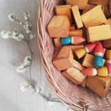 Holzbausteine und Grapat Nins Tomtens Holzzwerge liegen in einem Korb aus Weide geflochten.