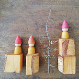 Vier Holzbausteine, darauf drei gelbe Holzzwerge von Grapat und ein Zweig mit Knospen.