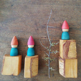 Vier Holzbausteine, darauf drei blaue Holzzwerge von Grapat und ein Zweig mit Knospen.