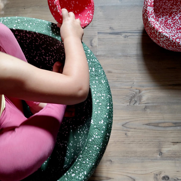 Ein Kind in einem grünen Grow Stapelstein spielt mit einem rot-weiß gesprenkelten Mini-Stapelstein, ein weiterer Original-Stapelstein liegt da, alle Teil des Limited Stapelstein®Blush Special Triology Set.