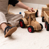 Der Fagus Schlepper Spielzeugtraktor aus Holz. Ein Kleinkind greift mit seiner Hand auf das Dach des Holztraktors.