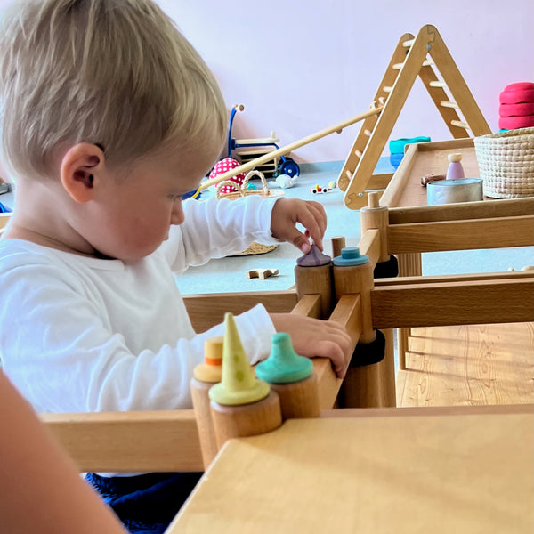 ein Kind steckt sehr konzentriert kleine, bemalte Holzteile aus dem Set Fancy Nins von Grapat in Löcher eines Holzregales