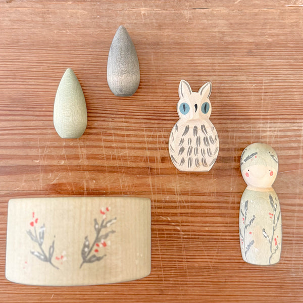 Hello Winter von Grapat & Ostheimer: eine Holzschale, mit zarten Winterzweigen bemalt, rechts davon eine Grapat Nins Holzfigur, eine weiße Schneeeule von Ostheimer und zwei kegelfömige Mandalas.