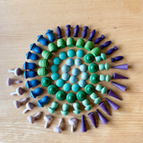 Eine kleine, buntlasierte Mandalaform in Blau-, Grau- und Lilatönen. Die Form in der die Mandalasteine gelegt sind, ist einer Schnecke nachempfunden.