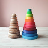 Ein Blick von vorne auf 2 verschiedene Stapeltuerme. Der linke hat runde Naturholzscheiben - ohne Farbe.Die einzelnen Ringe 10 an der zahl sind zwar flach gearbeitet, aber die Kanten geschmeidig abgerundet.  Daneben steht der Scheibenturm von Grimms in Regenbogenfarben. Dieser ist ein Stueck hoeher, hat etwas mehr Durchmesser und die buntlasierten Scheiben sind an den Aussenkanten eher kantig, als abgerundet.