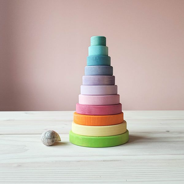 Ein Blick von vorne auf den Grimms Scheibenturm in Pastellfarben. Man sieht 11 von unten nach oben kleiner werdene Holzscheiben in Pastelltoenen. Davor liegt ein Schneckenhaus einer Weinbergschnecke als Groessenvergleich.