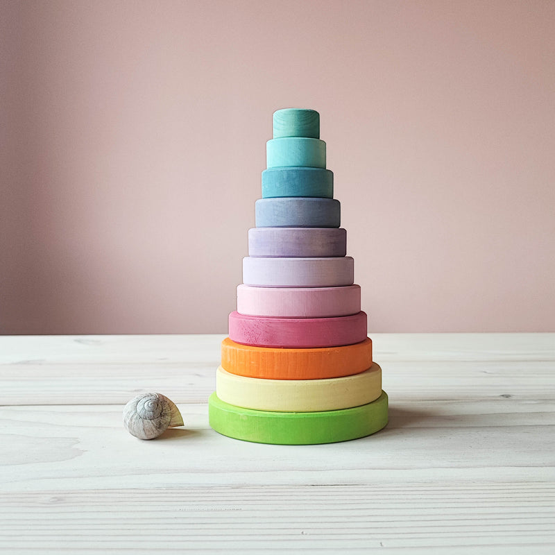 Ein Blick von vorne auf den Grimms Scheibenturm in Pastellfarben. Man sieht 11 von unten nach oben kleiner werdene Holzscheiben in Pastelltoenen. Davor liegt ein Schneckenhaus einer Weinbergschnecke als Groessenvergleich.