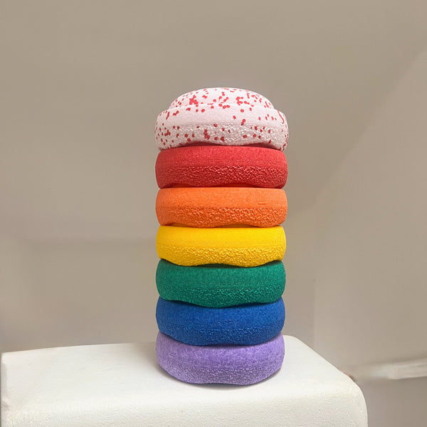 6 kleine Steine des Stapelstein MINI Regenbogen Set gestapelt, ganz oben drauf ein siebter Mini-Stein, nämlich Confetti Blush in der weihnachtlichen Edition mit roten Sprenkeln.