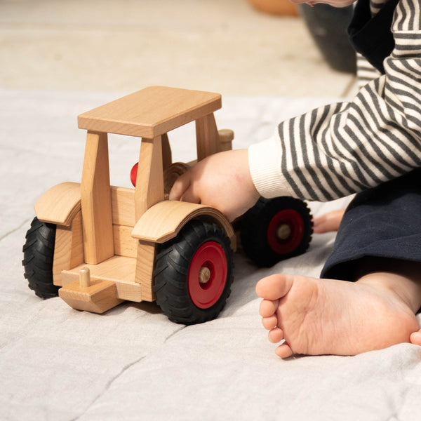 Der Fagus Schlepper Spieltraktor aus Holz, ein Baby sitzt daneben und spielt damit.