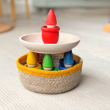 Das Kokomoo Bunte Zwerge Spielset für Babys ab 1 Jahr mit in einem Jutekorb mit gelbem Rand, einer Holzschale und den Grapat Mates und Grapat Tomtens in Regenbogenfarben.