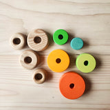 Ein Blick von oben auf 4 unterschiedlich grosse runde Holzscheiben mit Loch. Rechts davon liegen 5 bunte runte Scheiben vom Grimms Scheibenturm.