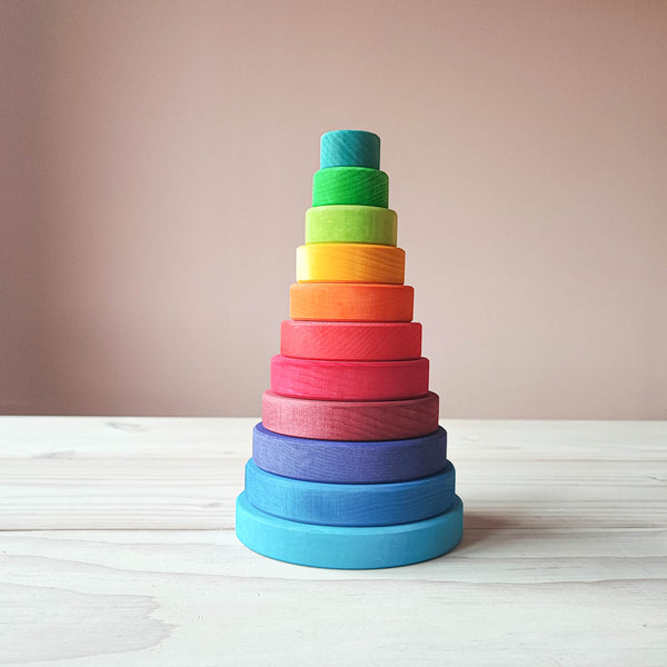 man sieht den bunten Scheibenturm von Grimms. Ein runder Stapelturm in Regenbogenfarben von helblau, mittelblau, blaulila, weinrot, rot, dunkelorange, orange, gelb, hellgruen, gruen bis tuerkisblau. Von gross bis klein.