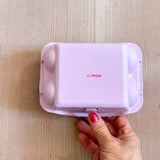 Ein zart lila Eierkarton, auf dem ein Kokomoo Schriftzug zu sehen ist.