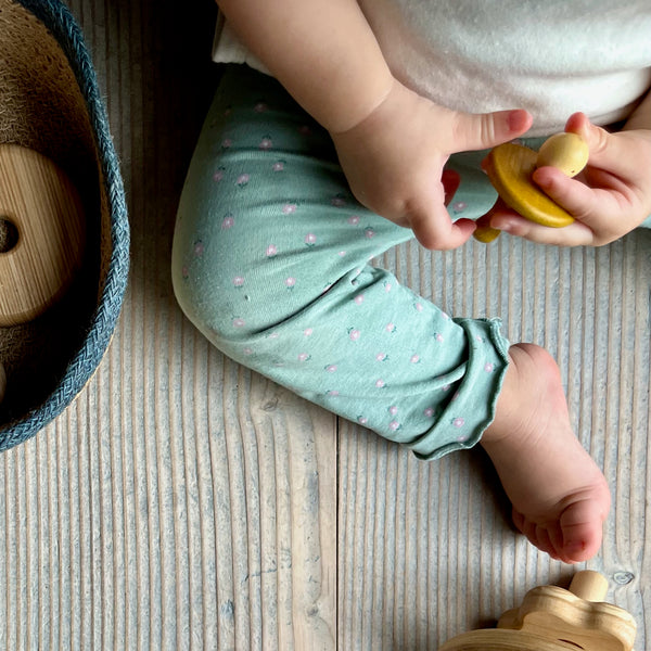 Ein sitzendes Baby hält einen Kreisel mit einem runden Kopf, ein Spielzeug-Teil von Grapat Schätze, in den Händen.