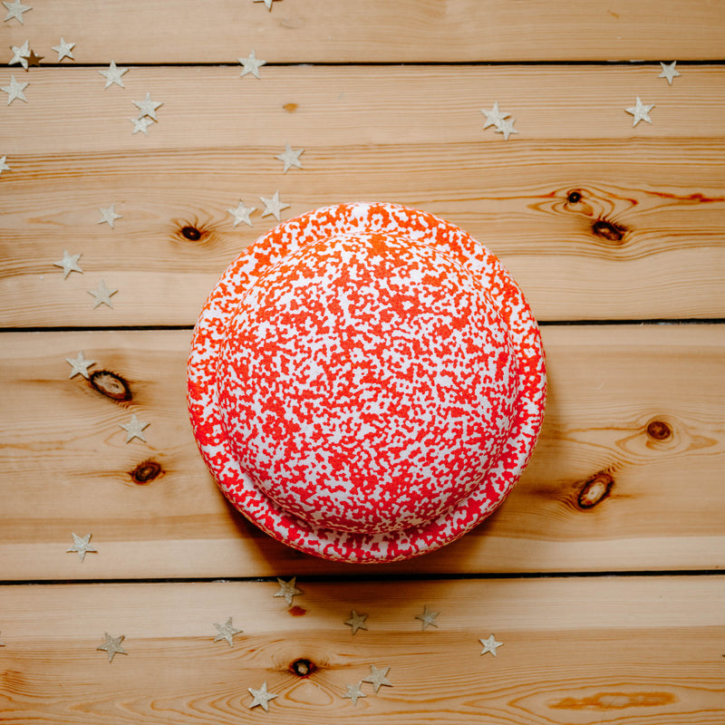 Draufsicht auf den rot-weiß geprenkelten Confetti Stapelstein Red& Blush auf einem Holzbretterboden liegend.