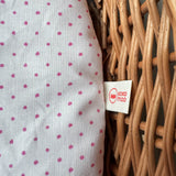 Detailansicht des Puppenbett Wichtelnests: rosa-getupfte Matratze mit Kokomoo-Logo und Weidengeflecht.