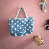 Die blaue Wendetasche mit weißen Tupfen  von Kokomoo hängt an einer rosa Wand.