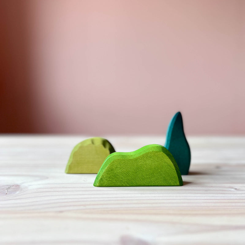 Verschieden große Holzstücke in Grüntönen stehen versetzt hintereinander, dass sind die Gebüsche von Ostheimer, beliebte Spielfiguren aus Holz für Kinder zum Spielen.