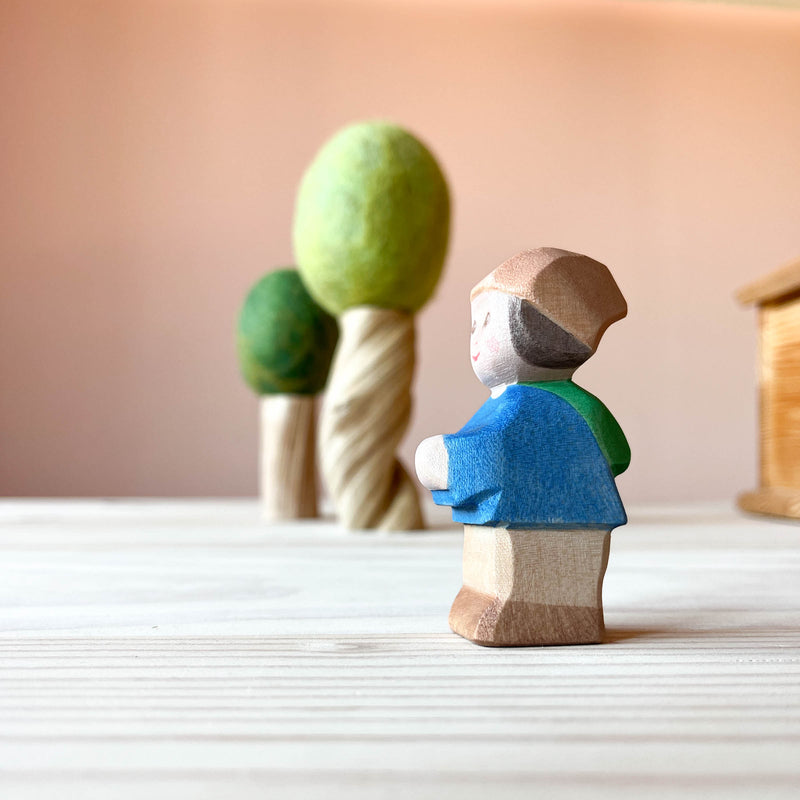 Im Vordergrund steht die Spielfigur Mo, ein kleiner Zwerg von Ostheimer und blickt seitlich nach links. Im Hintergrund stehen 2 Filzbäume.