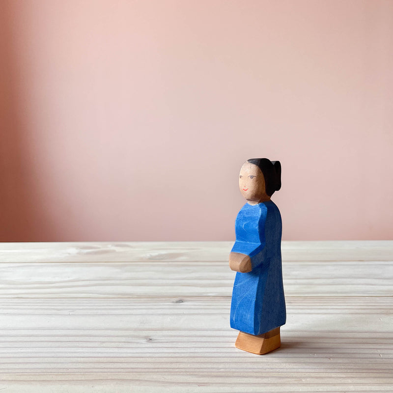 Ostheimer Holzfigur Mutter mit dunkler Hautfarbe und dunklem Haar, steht in blauem Kleid mit Blick seitlich nach vorne.