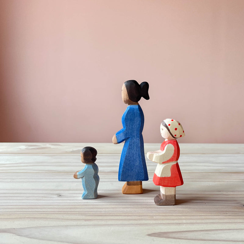 Ostheimer Spielfiguren aus Holz, nämlich ein Baby im Strampler, eine Frau und ein Mädchen mit rotem Kleid, weißer Schürze und Kopftuch mit Punkten darauf.