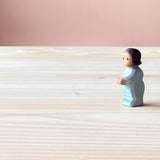 Die Ostheimer Spielfigur Wickelkind steht am rechten Rand des Bildes auf einer Holzplatte und schaut nach links. 