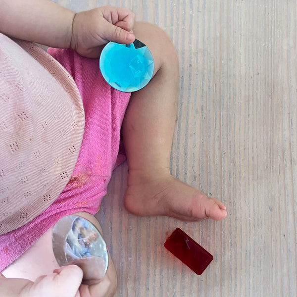 Ein Baby hält in seiner linken Hand einen blauen Riesenfunkelstein und in der rechten einen weißen. 