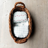 Das lichtblaue Wichtelnest von Kokomoo: ein ovales Weidenkörbchen als Puppenbett mit hellblau getupfter Matratze, blau-weiß karierter Decke und einem Puppenpolster mit Blümchenmuster.