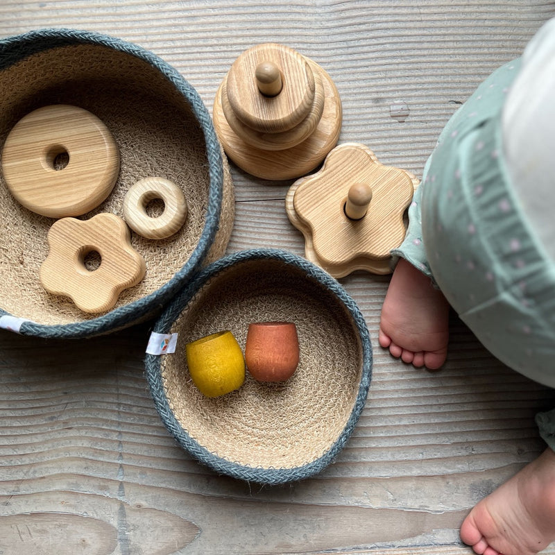 Kokomoo Spielset für Babys ab 1 Jahr. Die Spielmaterialien sind auf 2 Jutekörbe verteilt, daneben kniet ein Baby.