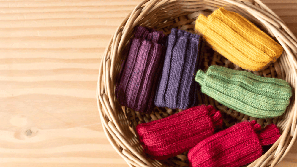In einem kleinen Körbchen aus Weide liegen sechs Paar Stulpen für Babys und Kleinkinder von Kokomoo in herbstlichen Farben.