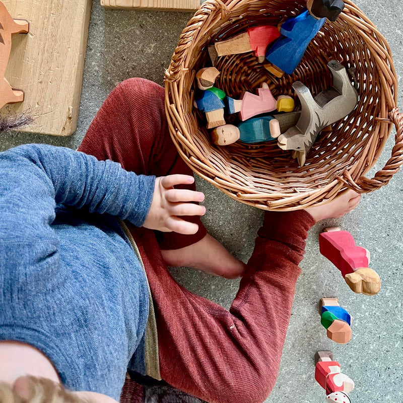 Ein Korb gefüllt mit Ostheimer Spielfiguren aus Holz, ein Kind spielt damit, daneben große Holzbretter und ein Ostheimer Holzpferd.