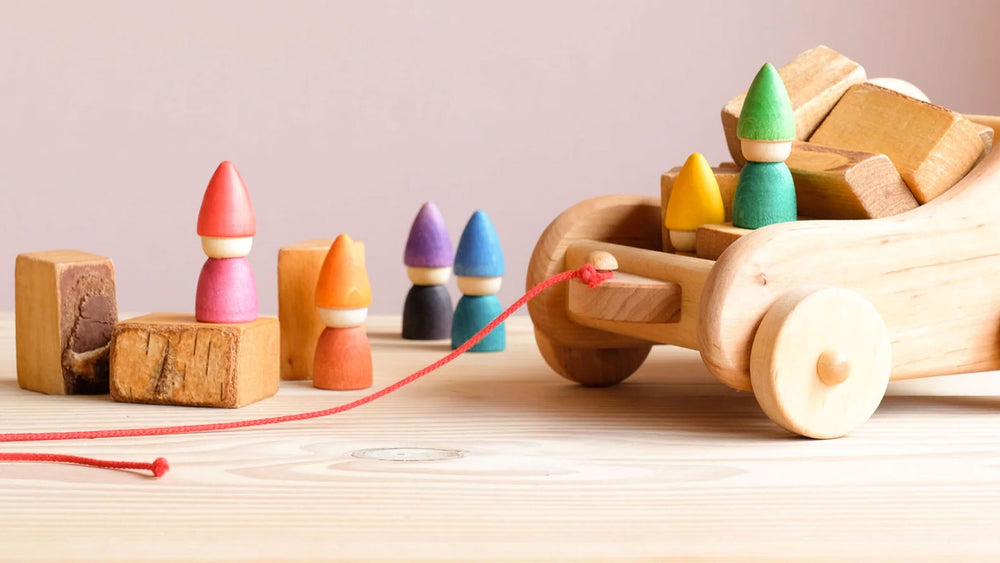 Ein Nachziehauto aus Holz gefüllt mit Holzbausteinen und Zwergen, rundheru auch Holzklötze und bunte Zwerge Spielfiguren.