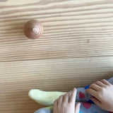 Die Rassel Kugelrund, gesehen von oben, kreiselt vor einem Kind im Kreis herum. Dann Zeitlupe. Das Kind streckt den Arm nach der Rassel aus, hält diese aber nicht an, sondern bleibt in der Beobachtung.