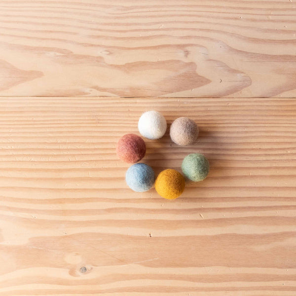 Sieben kleine Filzkugeln von Papoose Toys in verschiedenen Farben im Kreis aufgelegt.