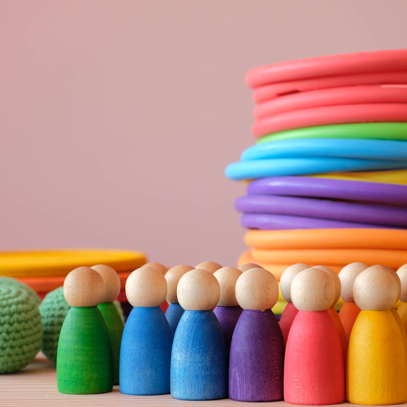 Grapat Nins Holzfiguren in den sechs Regenbogenfarben, dahinter bunte Motorikringe.