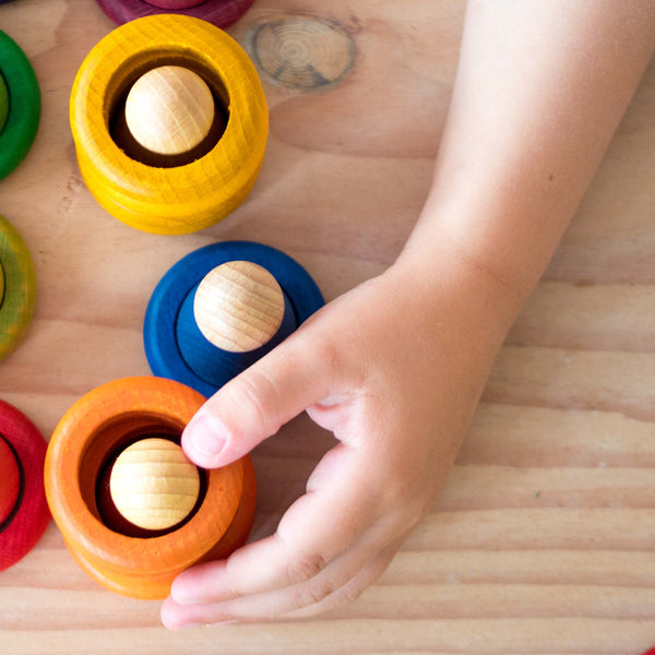 Eine Kinderhand spielt mit Grapat "Nins, Rings & Coins" in gelb, orange und blau. Die Holzfiguren sind in die gestapelten Ringe gesteckt.