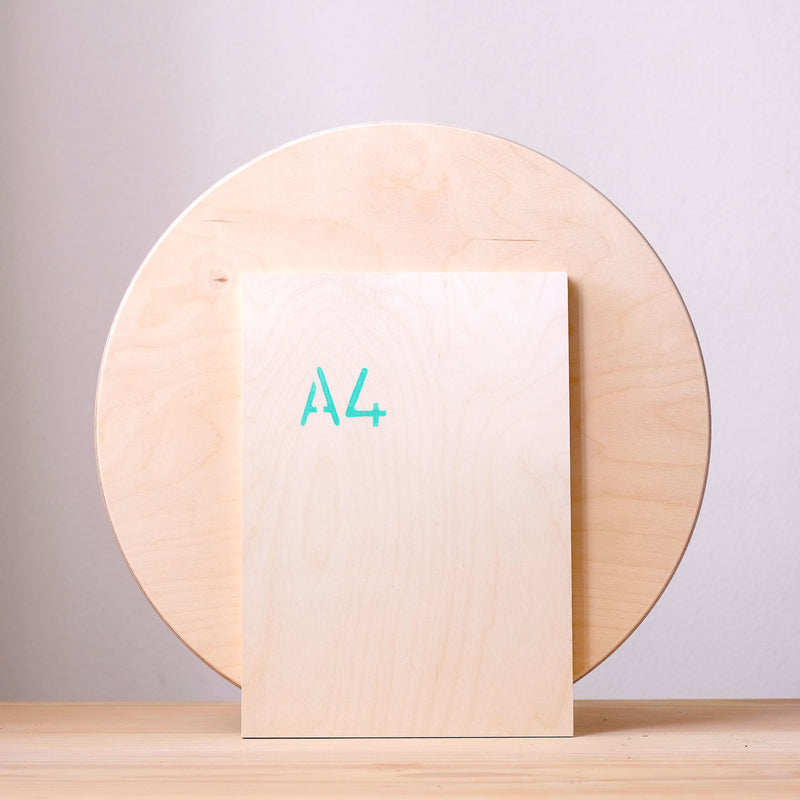 Vor der großen, runden Holzplatte von Grapat steht eine Platte in der Groesse DIN A4, so wird der Durchmesser der Holzplatte von 38 Zentimeter gut veranschaulicht.