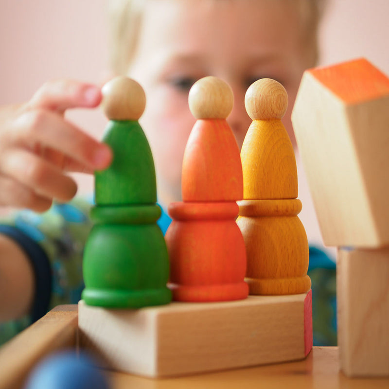 Ein Kind spielt mit grünem, orangen und gelben Grapat Spielmaterialien aus Holz.