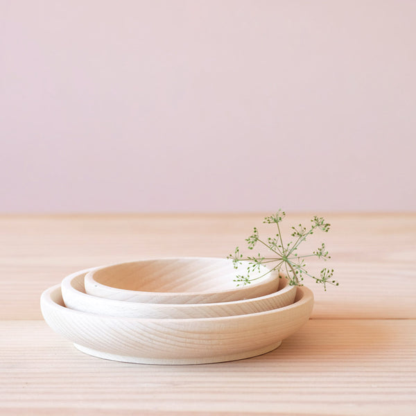 Man sieht ein 3er Holzschalen-Set aus unbehandeltem Holz. Alle 3 Schalen stehen ineinandergestapelt. Eine Bluete liegt darauf.